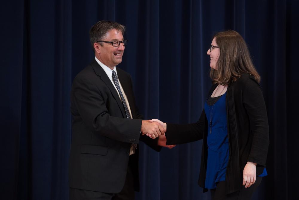 Doctor Smart shaking hands with an award receipient in a blue shirt and black sweater